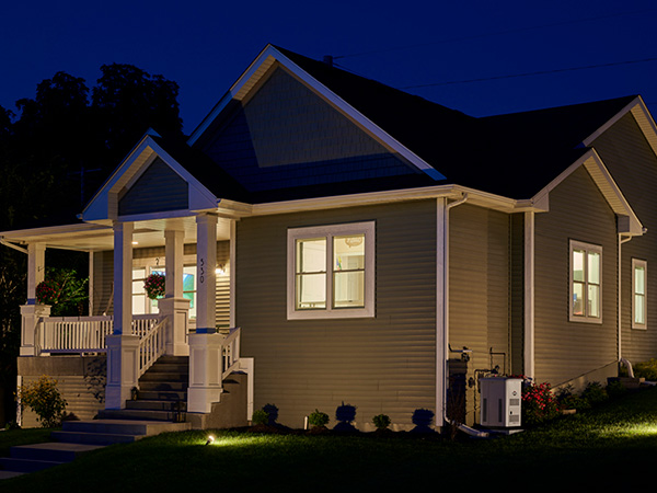 A standby generator next to a home with all its lights on at night. 