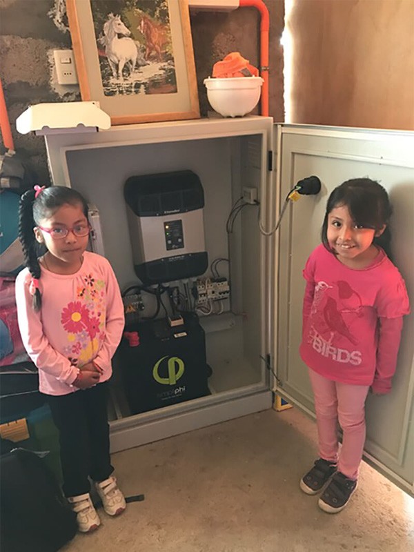 Two Chilean children standing next to cabinet entailing PHI battery